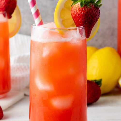 A glass of strawberry lemonade with ice, garnished with a slice of lemon and a whole strawberry.