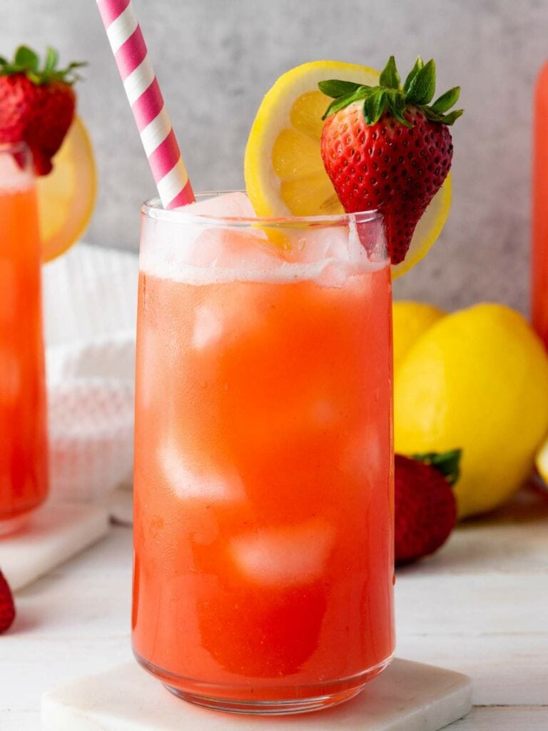 A glass of strawberry lemonade with ice, garnished with a slice of lemon and a whole strawberry.
