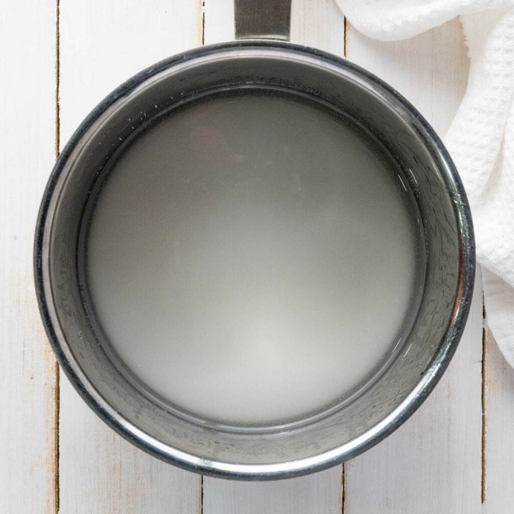 Top view of a metal pot containing a cloudy white liquid, placed on a white wooden surface.