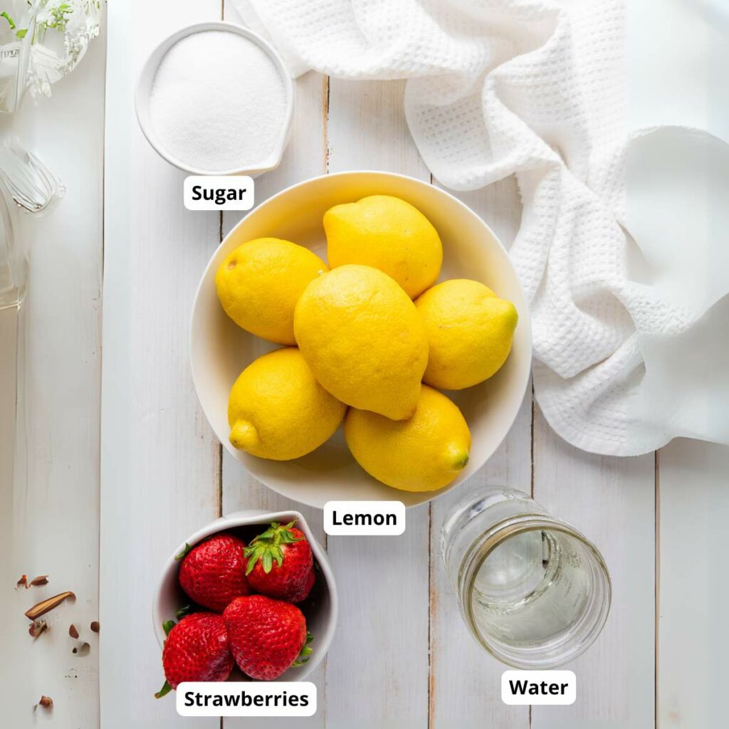 A bowl of lemons, a cup of strawberries, a glass of water, and a bowl of sugar on a white table with a white cloth.