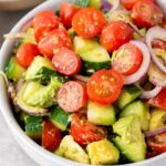 A bowl of salad containing sliced cherry tomatoes, cucumber, avocado, and red onion with a light dressing.