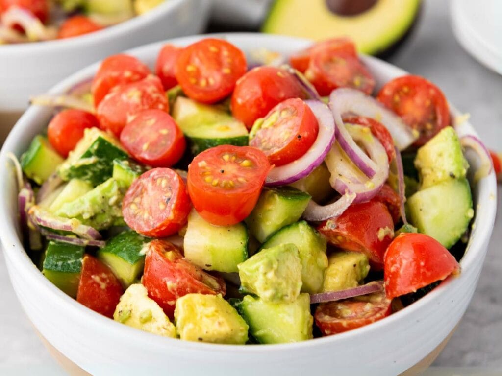 A bowl of salad with cherry tomatoes, cucumber, avocado, and red onion slices, mixed and ready to serve.