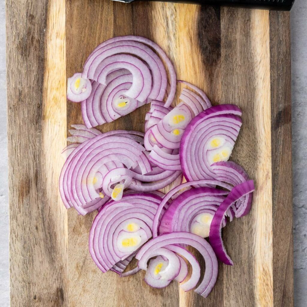 Thinly sliced red onions are arranged on a wooden cutting board.