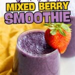 A glass of purple mixed berry smoothie with a whole strawberry garnish, set on a yellow cloth, with another smoothie in the background.