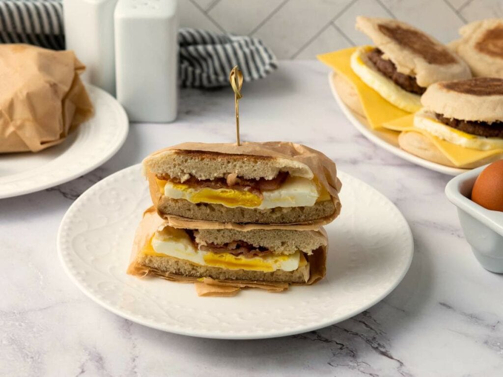 A breakfast sandwich with egg, cheese, and bacon cut in half, stacked on a white plate.
