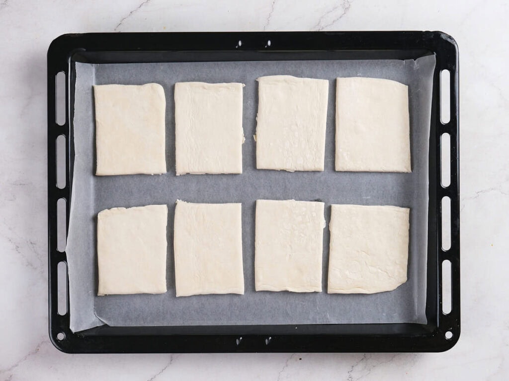 A baking tray lined with parchment paper holds eight rectangular pieces of uncooked dough arranged in two rows.