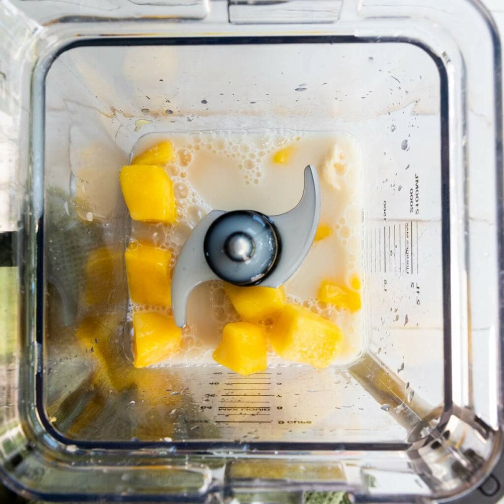 Cubed mango pieces and milk inside a blender, viewed from above.
