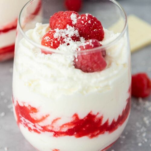 A glass filled with white chocolate mousse, topped with fresh raspberries and white chocolate shavings.