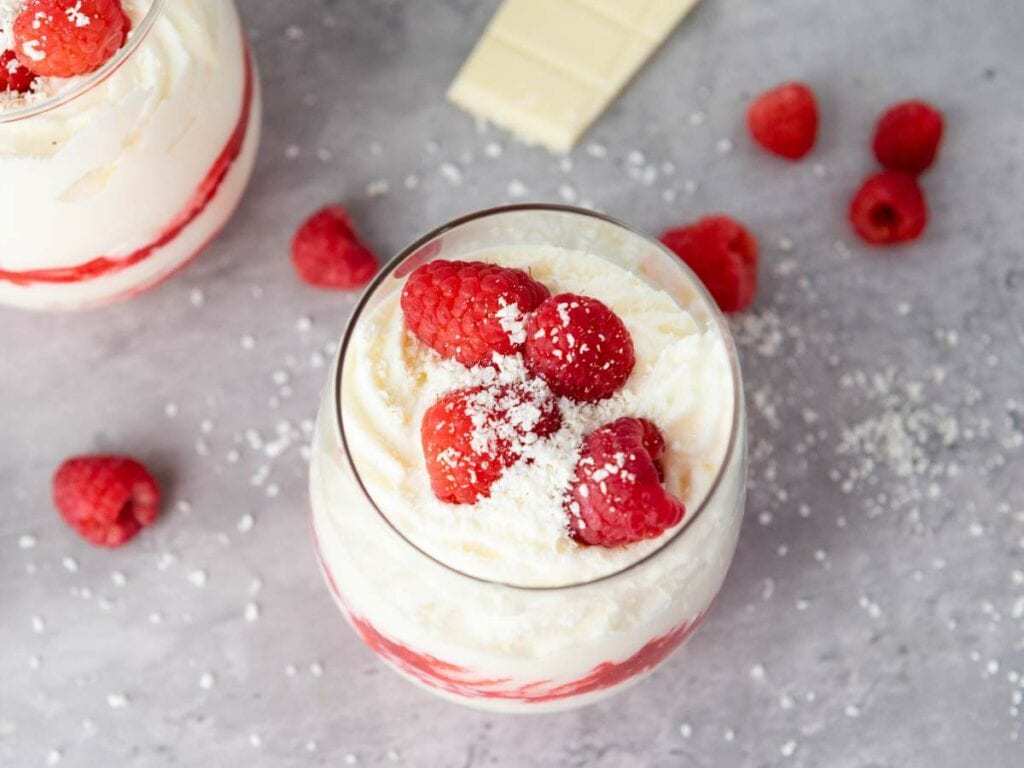 A glass of white chocolate mousses, topped with more raspberries and grated white chocolate.