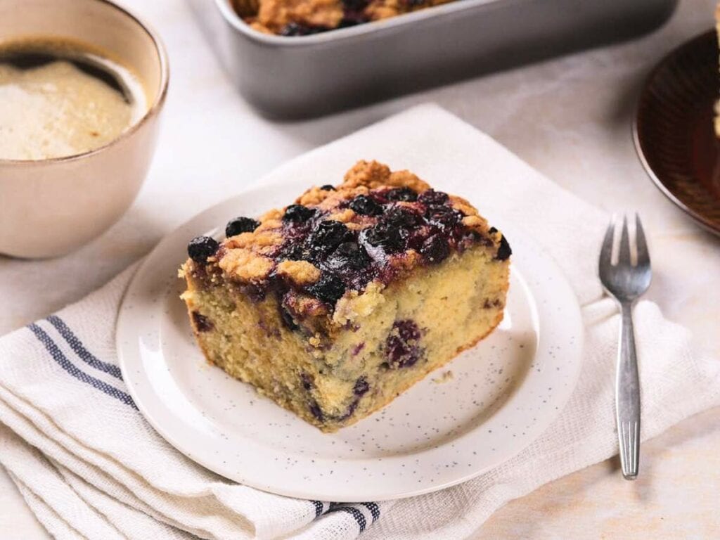 A slice of blueberry coffee cake sits on a white plate.