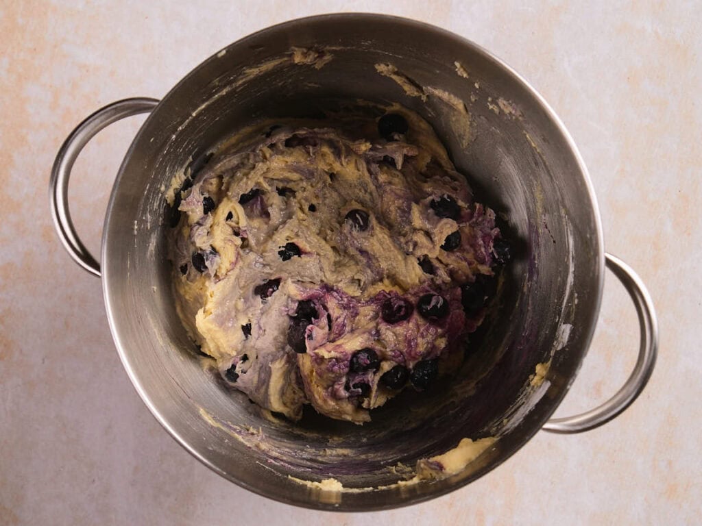 Stainless steel mixing bowl containing raw blueberry dough.