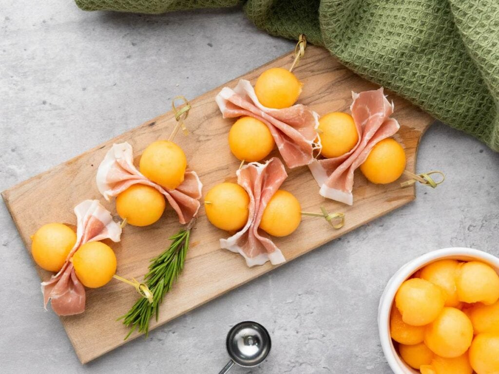 Skewers of cantaloupe prosciutto balls garnished with rosemary.
