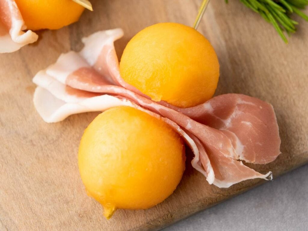 A skewer with two cantaloupe prosciutto balls.