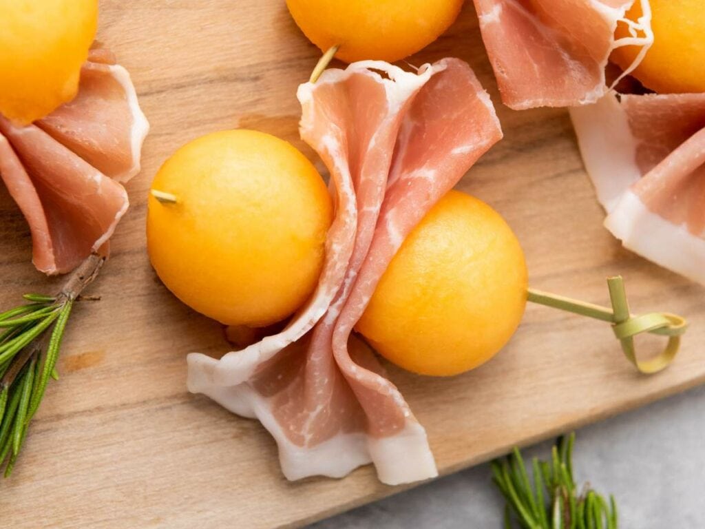Two cantaloupe prosciutto balls skewered with a toothpick.
