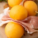 Three cantaloupe prosciutto balls and folded slices of prosciutto are skewered.