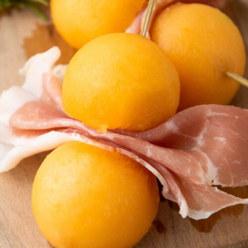 Three cantaloupe prosciutto balls and folded slices of prosciutto are skewered.