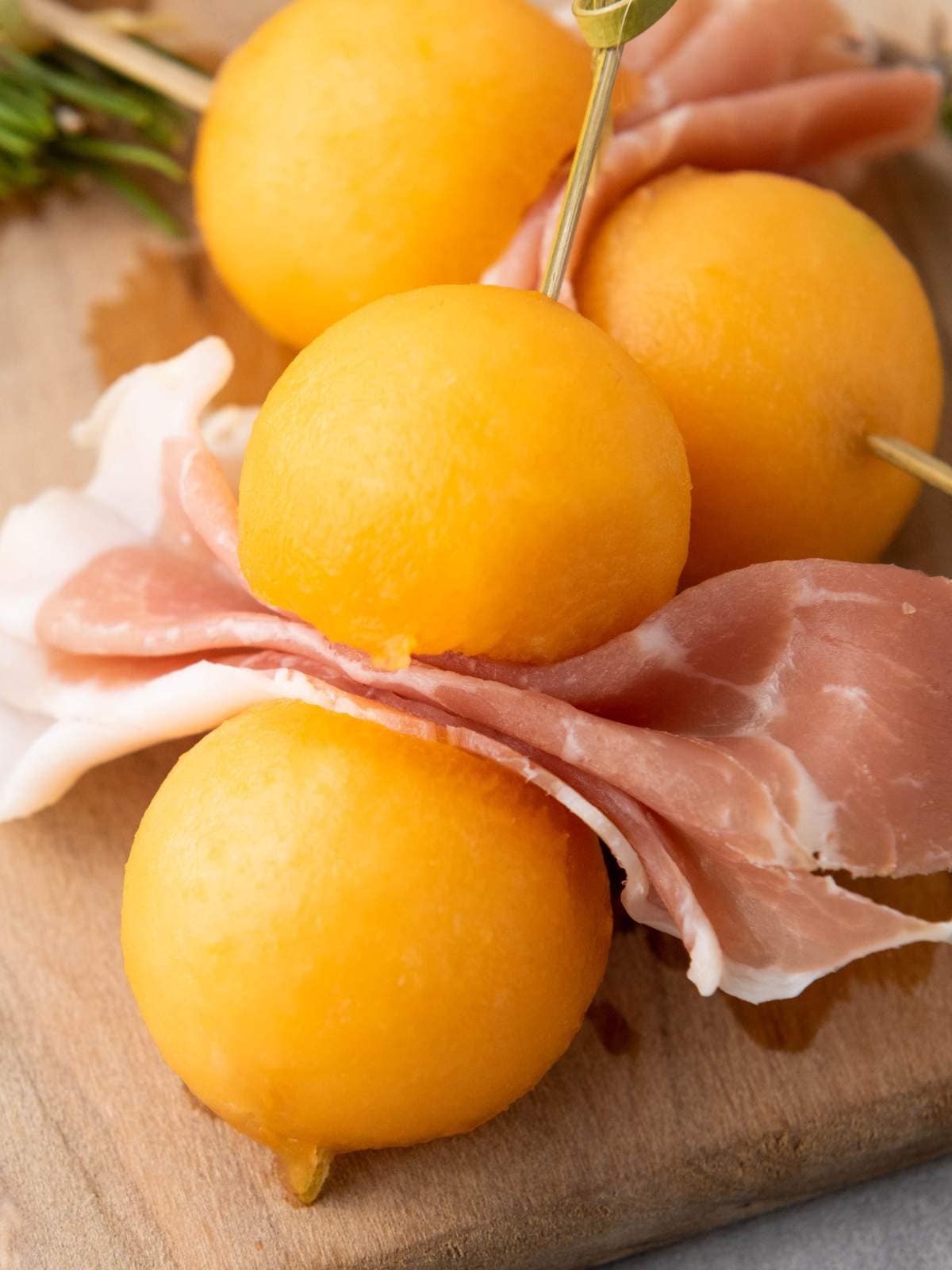 Three cantaloupe prosciutto balls and folded slices of prosciutto are skewered.