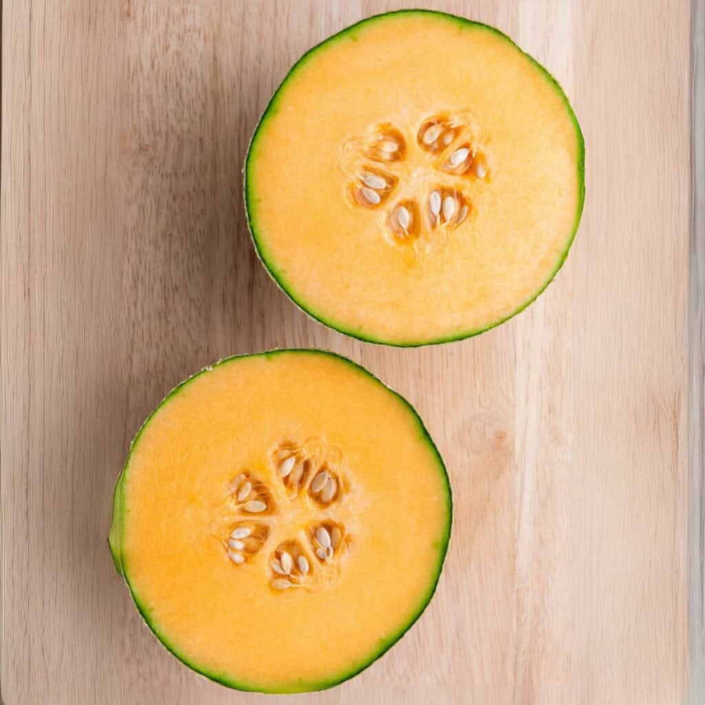 Two halves of a cantaloupe melon with orange flesh and seeds.