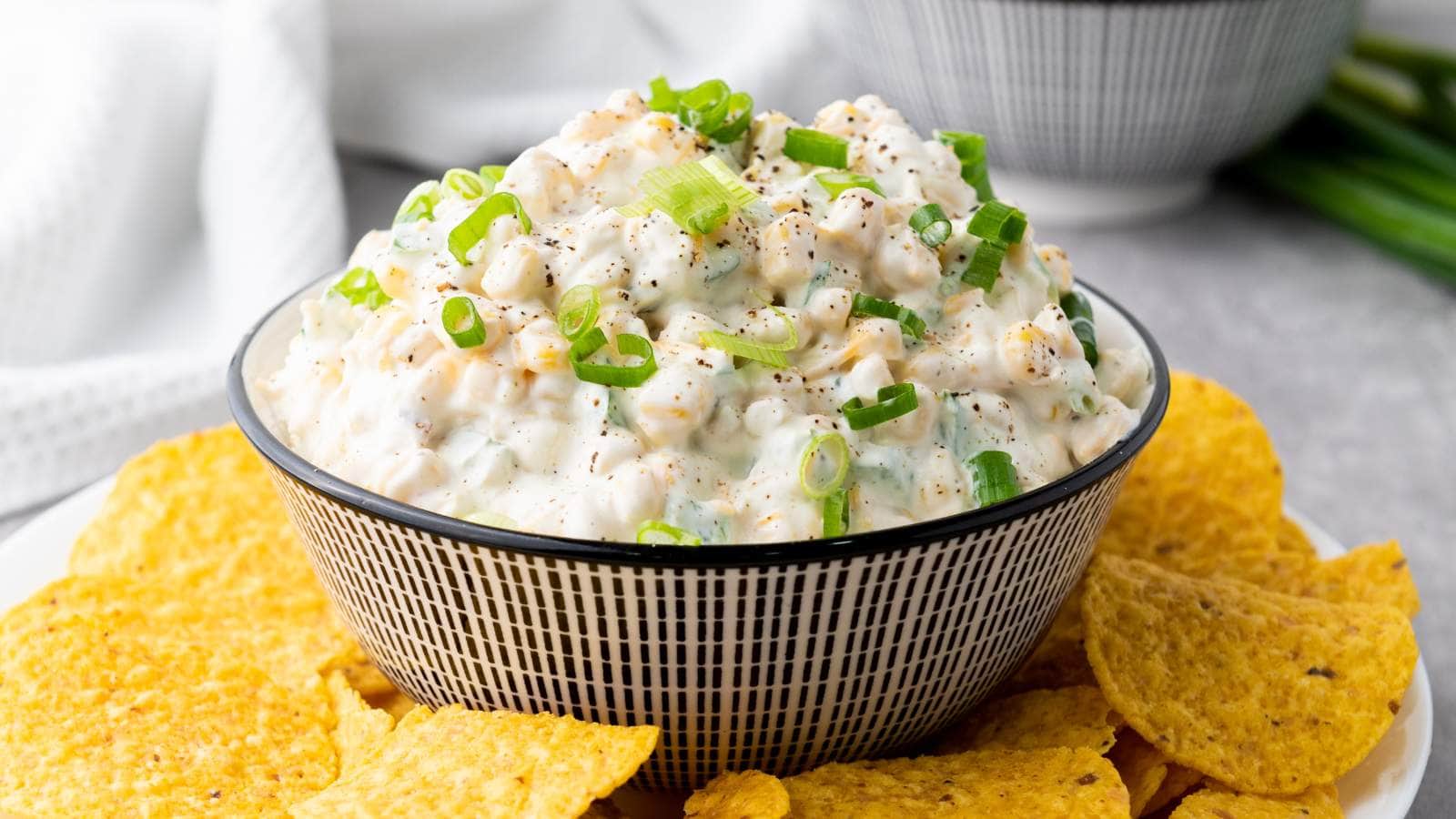 A creamy corn dip topped with chopped green onions, surrounded by tortilla chips.