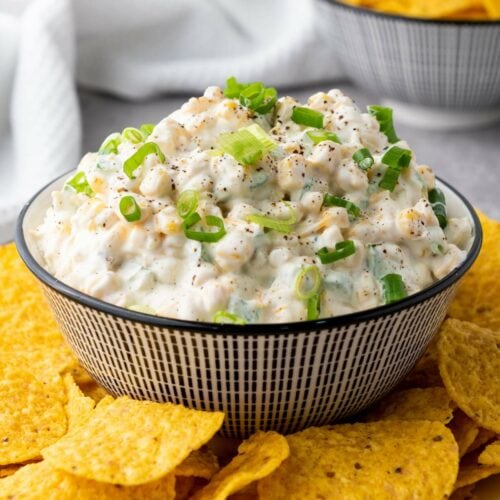 A bowl of creamy corn dip garnished with chopped green onions.