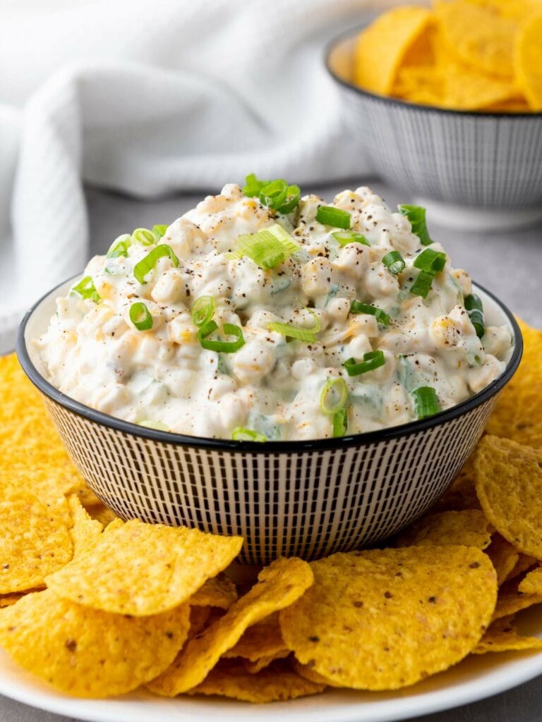 A bowl of creamy corn dip garnished with chopped green onions.