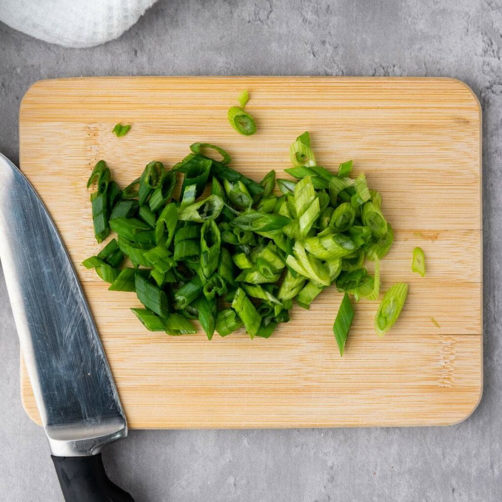 Chopped green onions on a wooden cutting board.