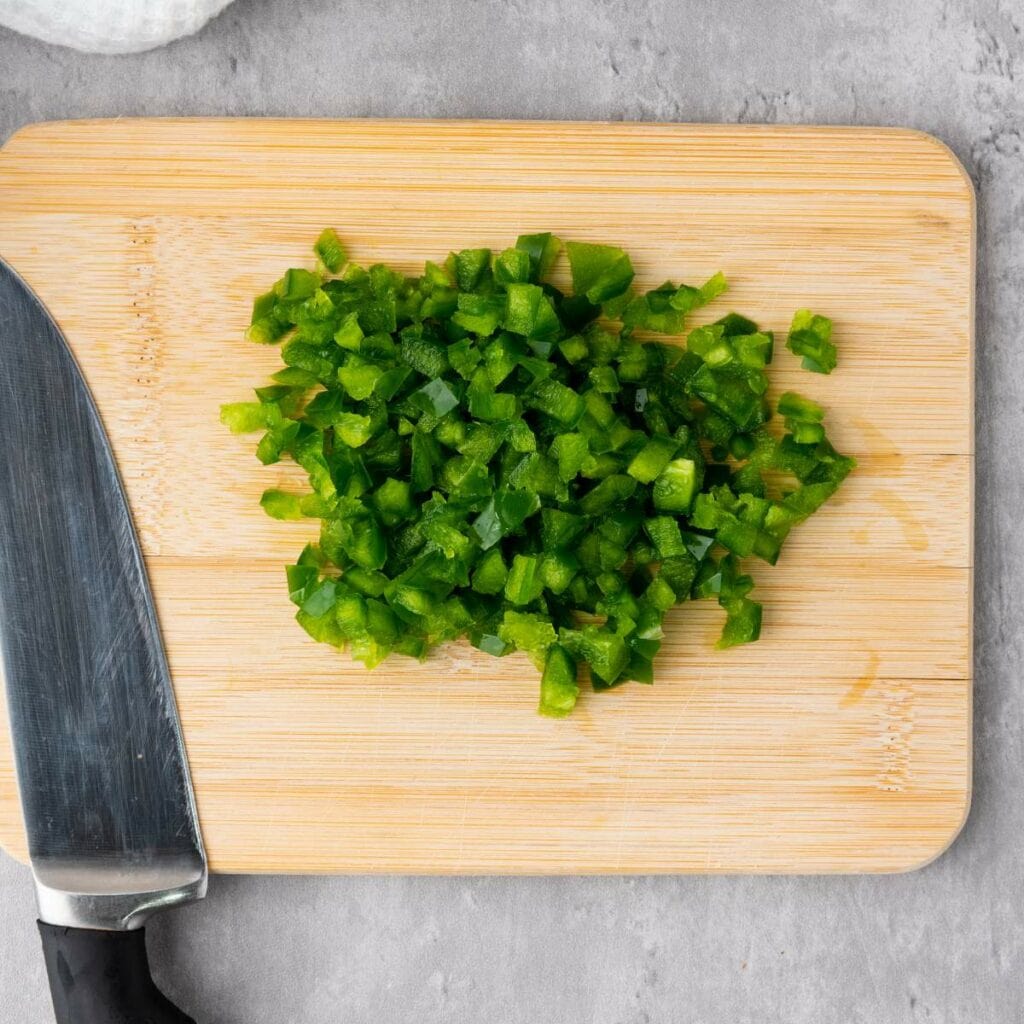 Diced green bell pepper on a wooden cutting board.