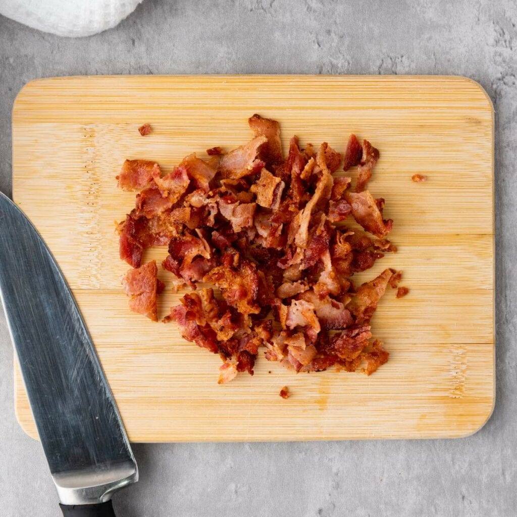 Chopped cooked bacon on a wooden cutting board.