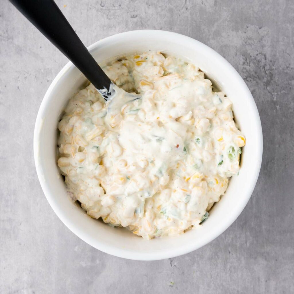 A white bowl filled with a creamy, mixed dip containing visible bits of corn and herb.