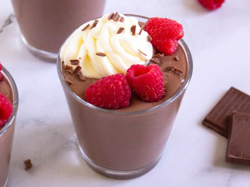 A cottage cheese pudding topped with whipped cream, chocolate shavings, and fresh raspberries.