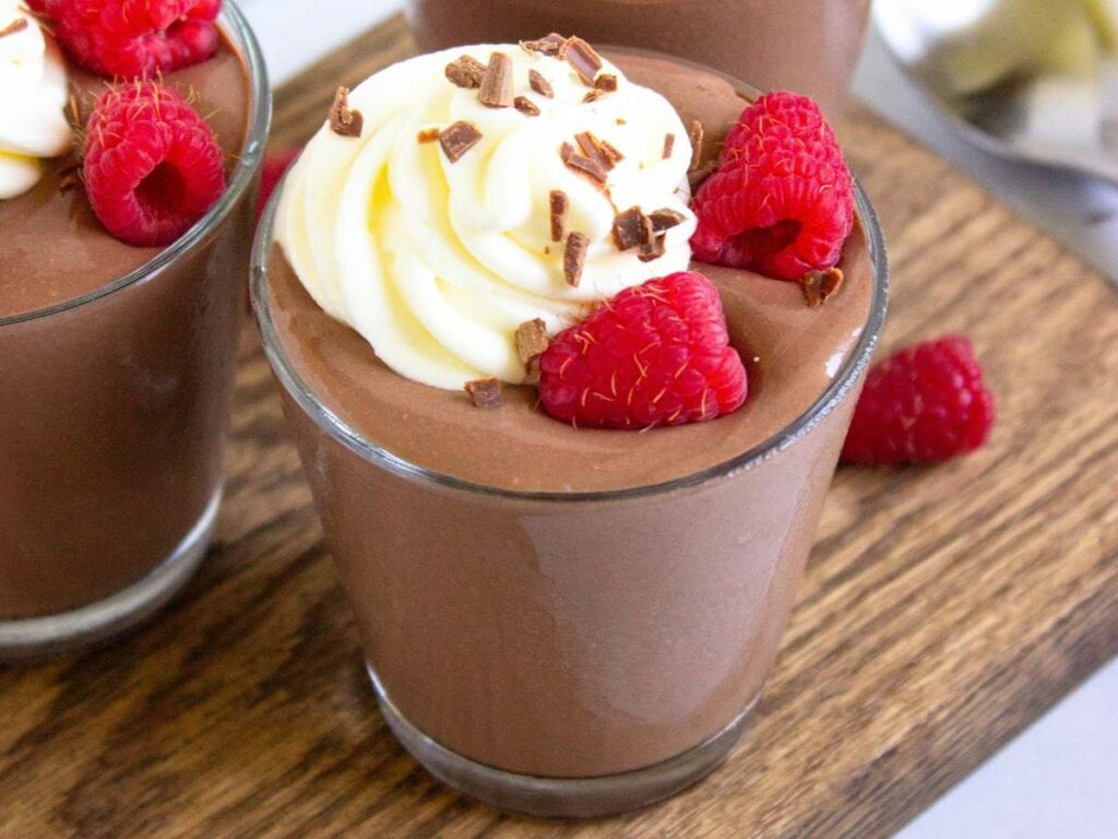 Glass of cottage cheese pudding topped with whipped cream, chocolate shavings, and fresh raspberries.