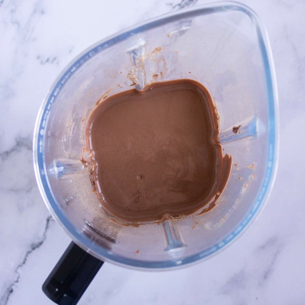 A blender containing a thick, light brown liquid mixture.