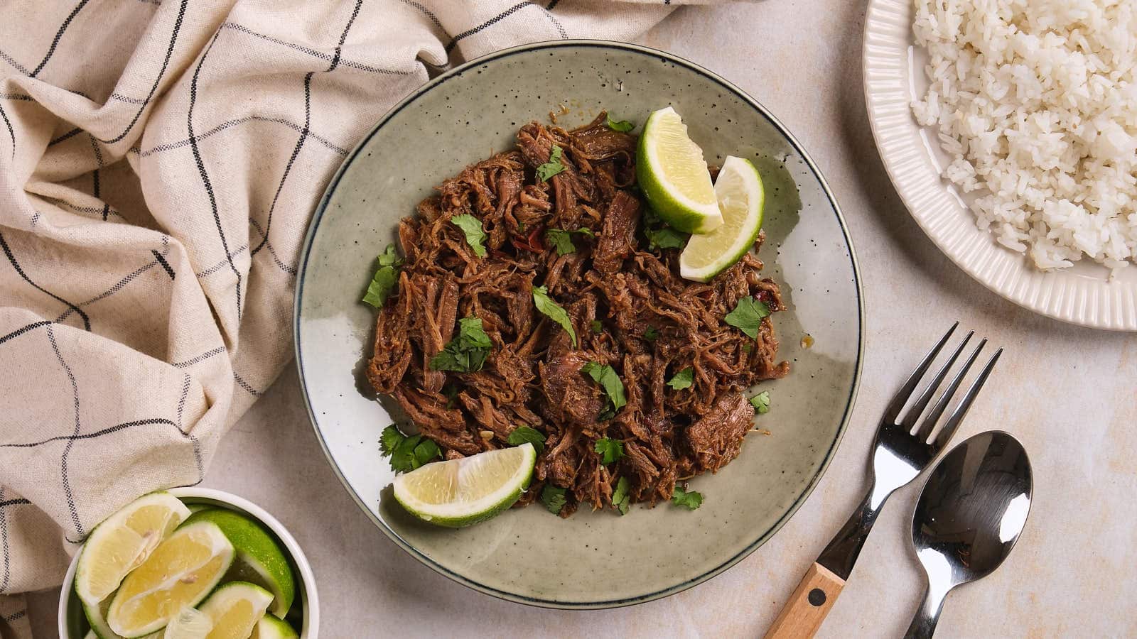A plate of barbacoa garnished with cilantro and lime wedges, served next to a bowl of lime slices.