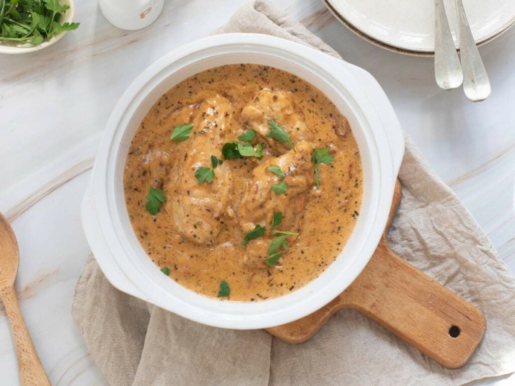 A white ceramic pot filled with marry me chicken skillet garnished with fresh parsley.