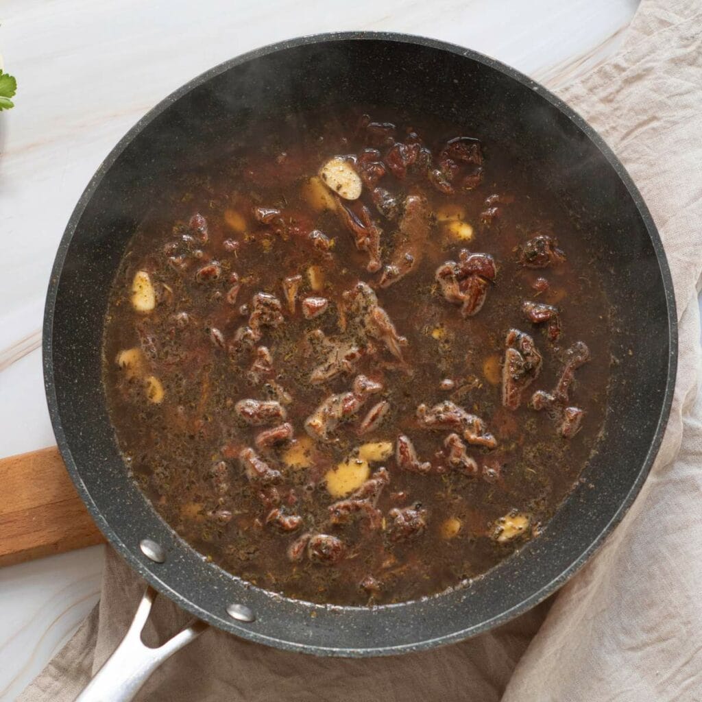 A skillet filled with dark brown liquid, mushrooms, and small pieces of meat.