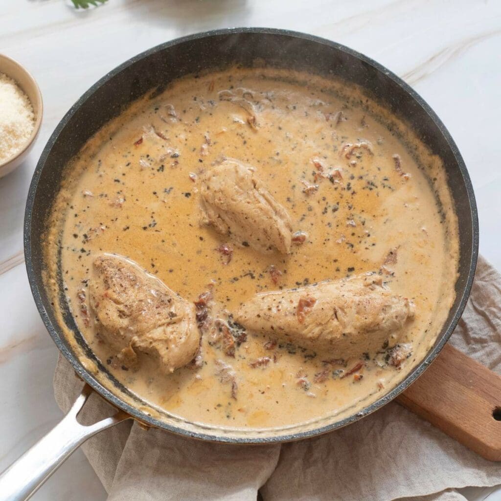 Three chicken breasts simmer in a creamy sauce.