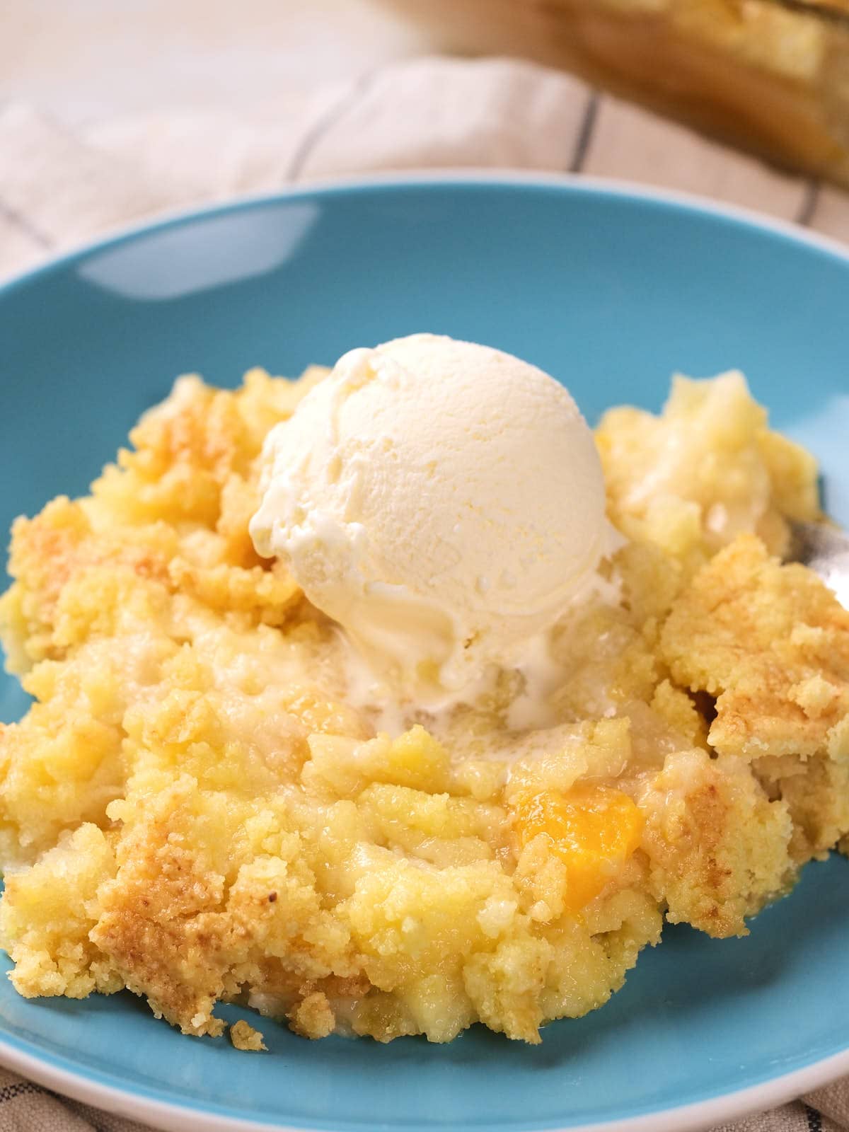 A serving of peach cobbler topped with a scoop of vanilla ice cream on a blue plate.