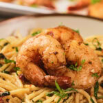 A savory dish of seasoned shrimp served over creamy pasta garnished with herbs.