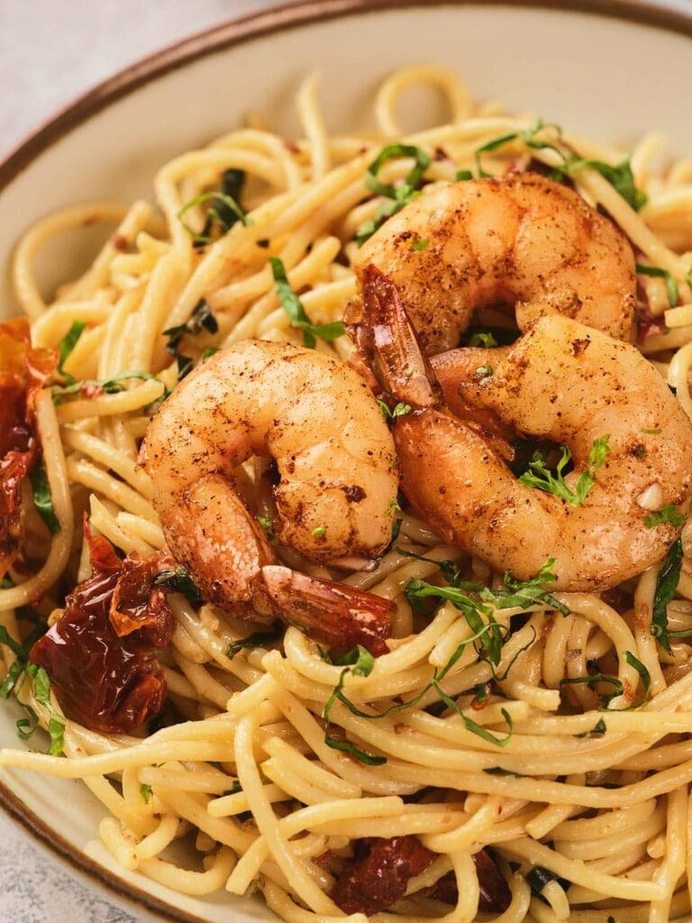 A plate of pasta topped with three baked shrimp garnished with herbs on a kitchen countertop.