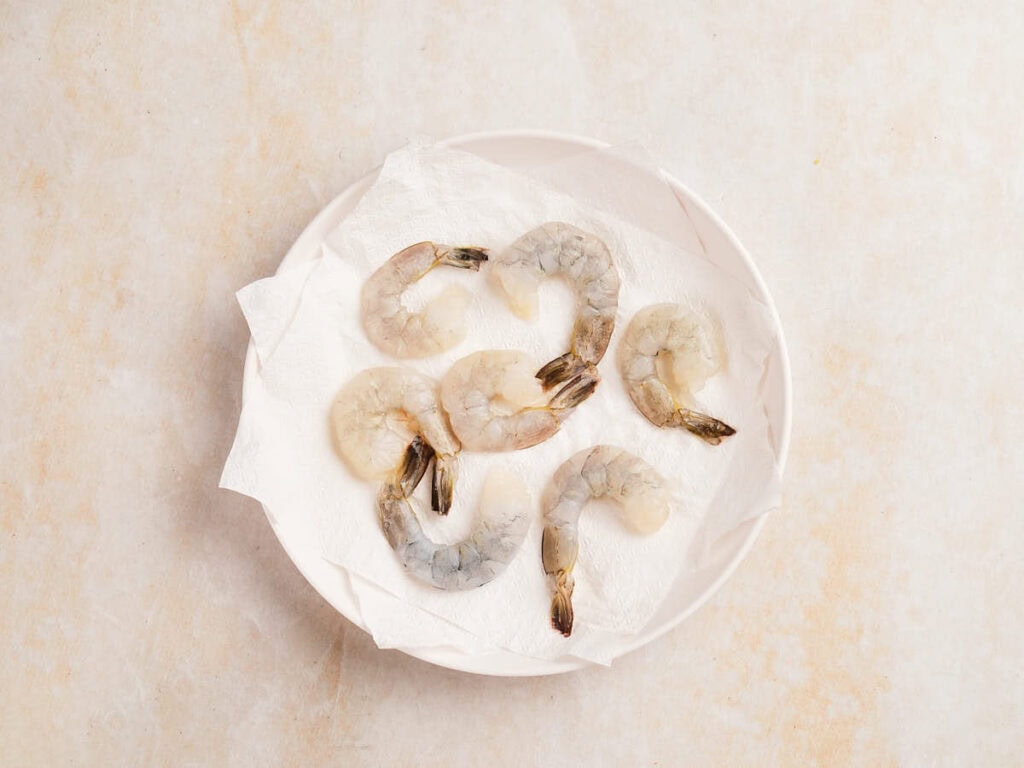 Raw, peeled shrimp arranged on a white paper towel in a white bowl.