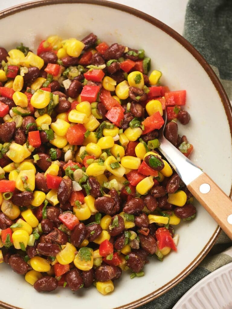 A bowl of black bean salad served with a wooden-handled spoon.