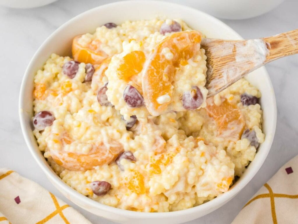 A spoonful of a creamy fruit salad with cool whip in a white bowl with colorful table napkin on the background.