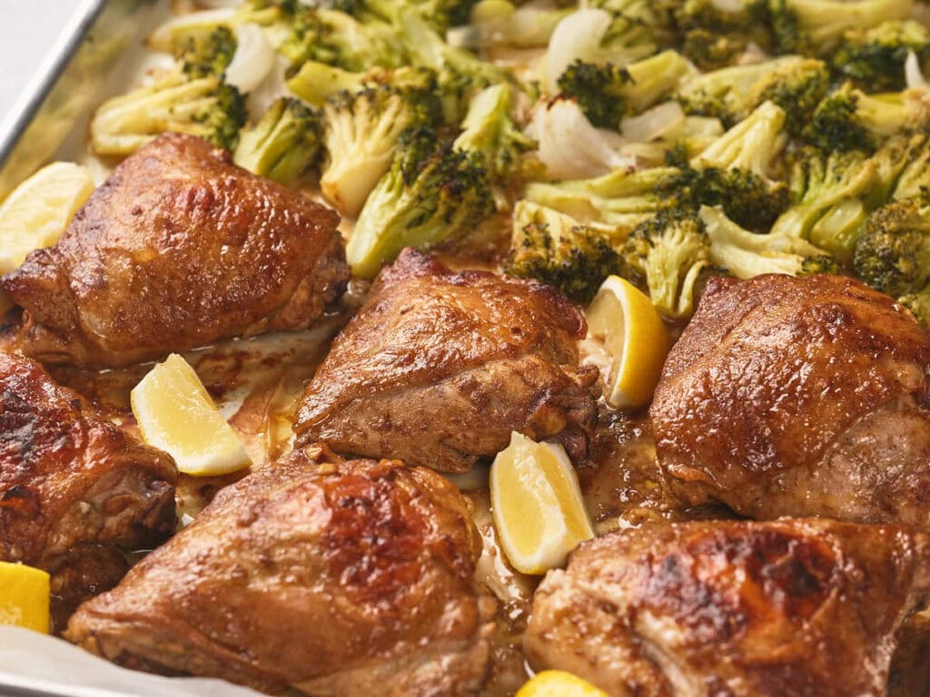 One pan chicken thighs with lemon wedges and broccoli florets.