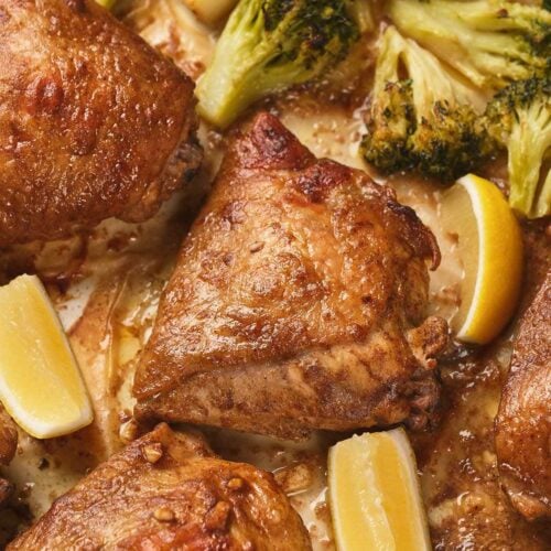One pan chicken thighs with crispy skin, broccoli florets, and lemon wedges.