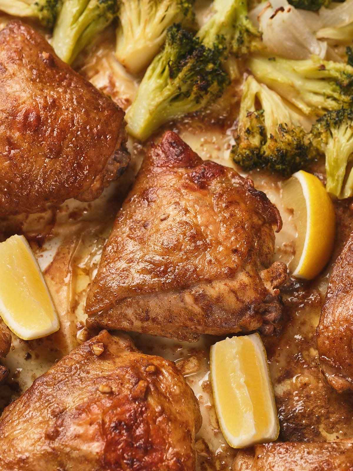 One pan chicken thighs with crispy skin, broccoli florets, and lemon wedges.