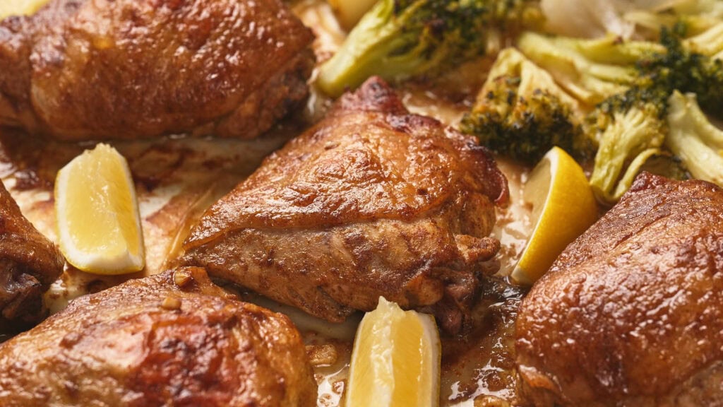 A chicken thighs with crispy skin, served with lemon wedges and broccoli.