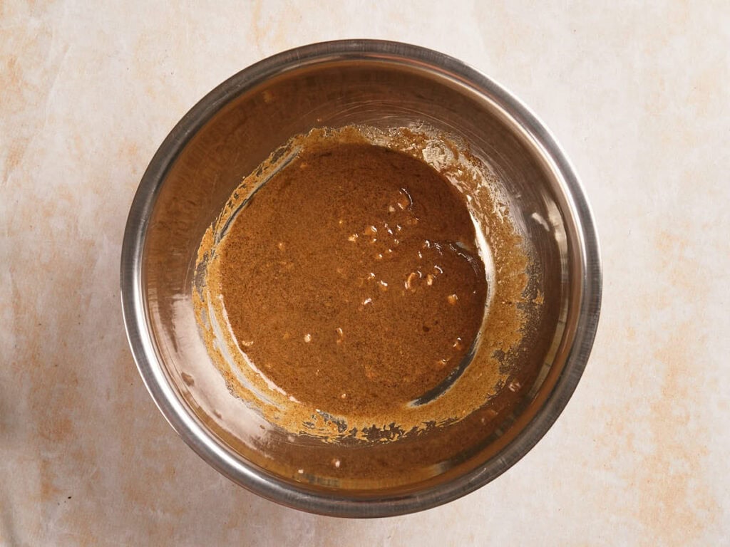 A stainless steel mixing bowl containing a light brown liquid mixture sits on a beige countertop.