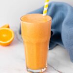A tall glass of orange carrot juice with a yellow-striped straw.