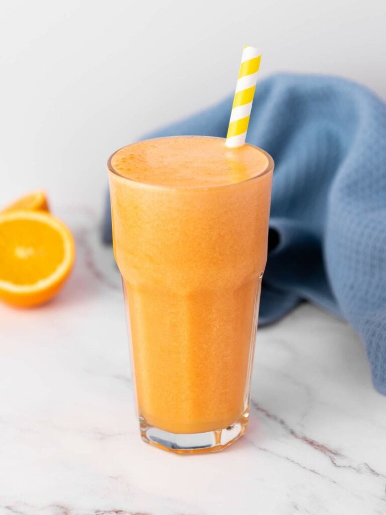 A tall glass of orange carrot juice with a yellow-striped straw.