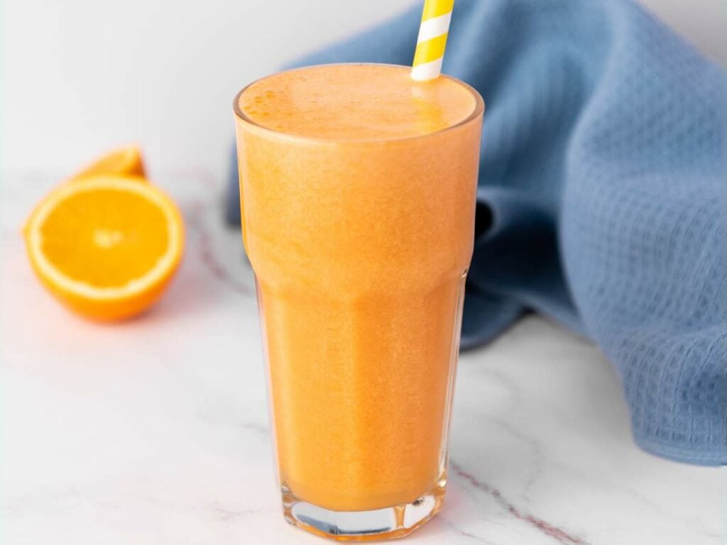 A glass of orange carrot juice with a yellow and white striped straw.